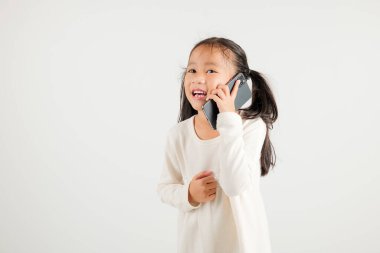 Mutlu Asyalı genç kız gülümsemesi heyecanlı konuşan akıllı cep telefonu stüdyosu beyaz arka planda izole edilmiş Tayland anaokulu çocuğu akıllı telefondan jest yapıyor.