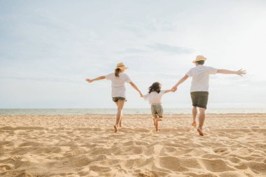 Mutlu Asyalı ebeveynler ve kızları sahilde eğleniyorlar. Kumda koşan ve rol yapan anne ve babalarıyla küçük kızlar. Olumlu aile aktivitesi