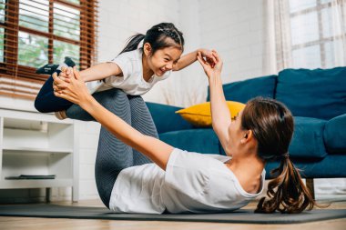 Bir anne ve kızı evde küçük kuş duruşuna odaklanarak eğlenceli bir yoga rutininin tadını çıkarıyorlar. Gülüşleri güven ve denge dolu uyumlu ve neşeli bir aile anını yansıtıyor..