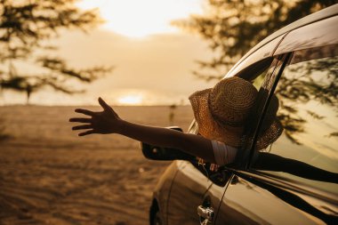 Şık şapkalı bir kadın gün batımında el sallayarak arabanın ön koltuğunda oturur ve rüzgarı hisseder. İyi hafta sonları. Plajda iyi tatiller. Yolculuk ve özgürlük kavramı