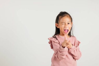 Neşeli Asyalı genç kız kameraya iki silah parmağı hareketi yapıyor. Dost canlısı ve küstah bir ifadeyle. Beyaz arka plana izole edilmiş, anaokulu çocuğu pozitif ve neşe yayıyor.