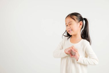 Gülümseyen Asyalı genç bir kız güven gösteriyor. Beyaz arka planda elleri ve parmakları olan bir kalp şekli yaratıyor. Anaokulu çocuğunun portresi Sevgililer Günü 'ne sevgilerini gönderiyor.