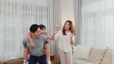 Aile Günü. Mutlu Asyalı baba, anne ve kız sırtımda taşıma ve uçuş oyunu oynamak oturma odasında uçak gibi görünüyor, evde mutlu aile hafta sonu.