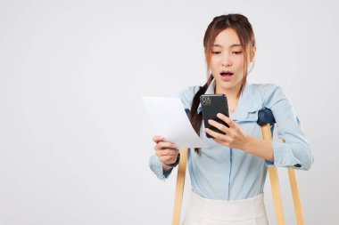 Koltuk değnekleri, ödemeyle vurgulanan, elinde telefon ve fatura kağıdı tutan endişeli bir kadını destekliyor. Koltuk değneklerine yaslanarak, kazadan sonra mali karışıklıkla boğulmuş hissediyor. izole stüdyo beyaz arkaplan