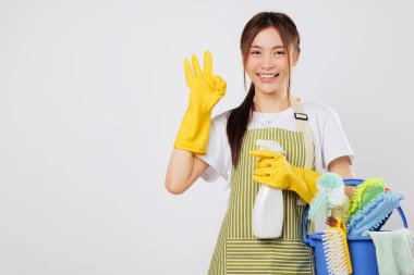 Önlük ve eldiven giyen, temizlik malzemesi dolu kova tutan ve kaliteli jest yapan profesyonel temizlikçi kadın. izole stüdyo beyaz arkaplan