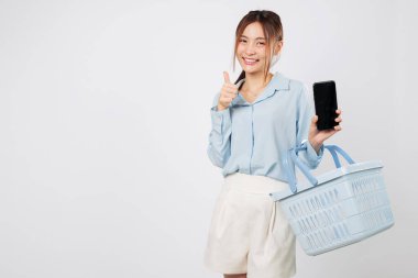 Market sepeti ve cep telefonuyla gülümseyen Asyalı kadın, süpermarkette telefon ekranlı alışveriş deneyimi ve online alışveriş neşesi gösteriyor. izole stüdyo beyaz arkaplan
