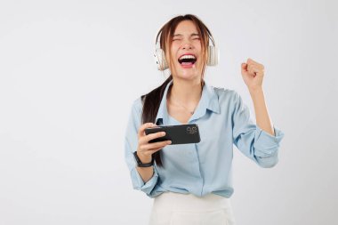 Oyun eğlencesi, heyecanlı Asyalı kadının cep telefonuyla yatay oynaması ve zafer dansında elini kaldırarak online anın tadını çıkarmasıyla başlıyor. izole stüdyo beyaz arkaplan