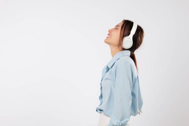 Kulaklıkla müzik dinleyen, gülümseyen, mutluluktan gözleri kapalı sakin müziğin getirdiği huzurlu duyguları ifade eden Asyalı genç bir kadının yan görüntüsü. izole stüdyo beyaz arkaplan