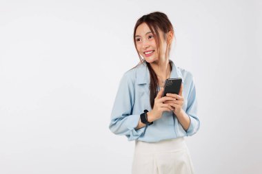 Heyecanlı Asyalı kadın gülümsüyor, elinde cep telefonuyla yan tarafa bakıyor. O, akıllı telefonundaki yeni başvurusundan memnun. izole stüdyo beyaz arkaplan