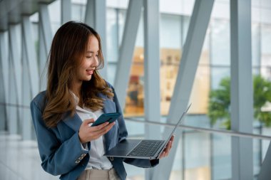 Modern iş kadını hareket halinde, havaalanında bağlı ve üretken kalmak için dizüstü bilgisayar ve cep telefonu kullanıyor..