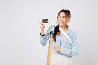 Koltuk değneği ve atel ile kırılan gülümseyen kadın sigorta onayından sonra kredi kartı ödemesini gösteriyor. Sigorta, sakatlık ve mali stresten sonra ödemeyi idare etmesine yardımcı oldu. izole edilmiş beyaz arkaplan