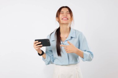 Mutlu genç Asyalı kadın elinde cep telefonu tutarken gülüyor. Gülümsüyor, yeni telefon cihazında terfi edeceği için heyecanlı. izole stüdyo beyaz arkaplan