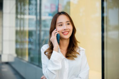 Resmi giyinmiş profesyonel bir kadın müşterisiyle telefonda konuşuyor. Ofisin yanında telefonla gülümseyen genç iş kadınının portresi. Modern iş için telefon iletişimi şarttır.