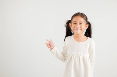 Mutlu Asya portresi gülümseyen küçük kız parmak boşluğunu gösteriyor, stüdyo resmi beyaz arka planda izole edilmiş, Tayland anaokulu çocuğu kopya alanı ile işaret ediyor.