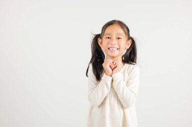 Gülümseyen Asyalı genç bir kız güven gösteriyor. Beyaz arka planda elleri ve parmakları olan bir kalp şekli yaratıyor. Anaokulu çocuğunun portresi Sevgililer Günü 'ne sevgilerini gönderiyor.