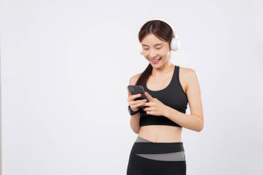 Kulaklığa bağlı telefon ve telefon, antrenman elbiseli spor Asyalı bir kadın antrenman seansını hızlandırmak için şarkı seçerken gülümsüyor. izole stüdyo beyaz arkaplan