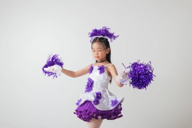 Mor ve beyaz üniformalı gülümseyen ponpon kız. Stüdyo fotoğrafı, temiz beyaz bir arkaplan. Gençlik enerjisi ve kutlama. Amigo kız.