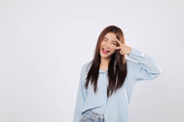 Göz kenarındaki zafer işareti heyecan, iyimserlik ve neşe gösteriyor. Mutlu Asyalı kadının yakalandığı zafer anı temiz beyaz bir arkaplan izole ederek pozitif enerji gösteriyor..