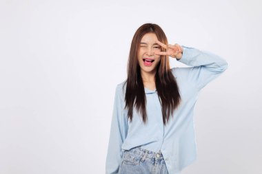 Göze yakın zafer parmakları güven ve eğlenceyi yansıtır. Asyalı bir kadın beyaz arka planda neşeyle izole edilmiş Ziyaretçi işareti ve heyecanı gösterirken zafer havası yakalamış..