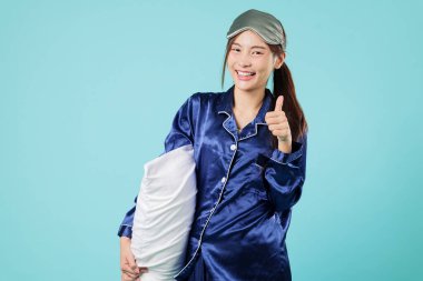 Mutlu genç Asyalı kadın yastık pijaması gülümse, başparmak işareti, iyi geceler uykusu için hazır, ve iyi bir işaret veriyor, rahatlatıcı, tatlı rüyalar ile pozitif uyku, izole stüdyo mavi arka plan