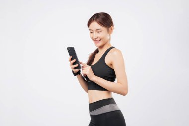 Telefonu elinde tutan ve telefon dinleyen bu sportif kadın spor kıyafetleriyle gülümseyen, spor salonunu kucaklayan, mobil uygulamalar ve sosyal yaşam tarzını tek bir şık bakışla benimseyen bir kadın. izole stüdyo beyaz arkaplan
