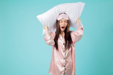 Pijamalı kadın uyumaya hazır, yastık başının üzerinde dinleniyor, gülümsüyor, iyi bir gece rüyası için sıkı tutunun, bu huzurlu sahne sizi uykunuza nazikçe yönlendirsin, vesikalıklar izole edilmiş stüdyo mavi arka plan