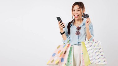 Gülümseyen Asyalı kadın çevrimiçi ödeme için telefon uygulaması kullanıyor, kredi kartı ve çanta tutuyor, alışveriş için heyecanlanıyor, telefonunu online alışveriş ve anlaşmalar için kullanıyor, izole edilmiş beyaz bir arka plan vesikalığı var.
