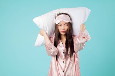 Yastıklı stresli Asyalı kadın horlama, pijama ve uyku maskesi yüzünden kulaklarını kapatıyor. Kötü ruh halini gösteriyor. Bu gece evde dinlenmeye çalışırken uykuya ihtiyacı var.