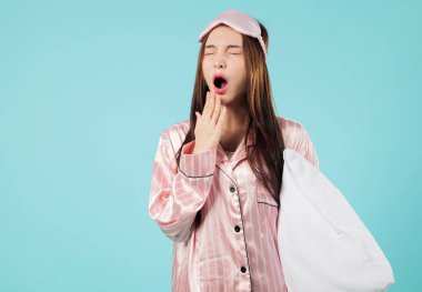 Uykulu Asyalı kadın yastıklı ve eli ağızlı çünkü daha fazla uykuya ihtiyacı var. Büyük bir sabah esnemesine kapılmış, daha uzun bir uyku umuduyla, büyük esneme, vesikalık, izole edilmiş stüdyo mavi arka plan.