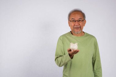 Beyaz domuz kumbarasını elinde tutan Asyalı yaşlı adamın portresi beyaz arka planda izole edilmiş, sorumluluk ve mali planlama kavramı, emeklilikten sonra tasarruf.