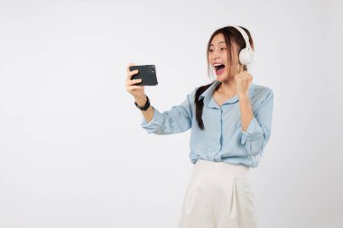 Cep telefonuyla oynanan oyun, kulaklık takmak, maçı kutlayan kadın elini kaldırmış ve heyecanlı bir yüz ifadesiyle her saniyenin tadını çıkarıyor. çevrimiçi izole edilmiş stüdyo beyaz arkaplan