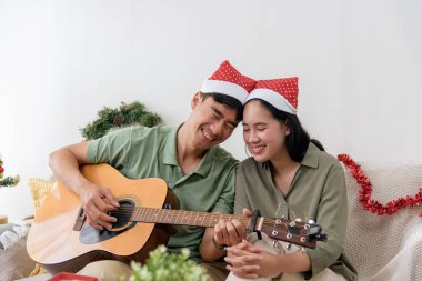 Christmas day brings happy couple much love, enjoying cozy winter holiday music, playing guitar and smiling together, warm celebration at home for christmas festivities.