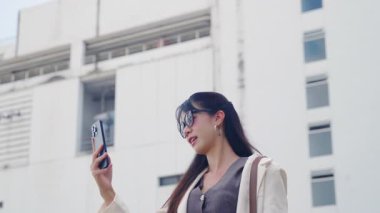 Şehir dışında gezmekten hoşlanan, akıllı telefonla etkileşime giren genç mutlu iş kadını, modern ofis mimarisi, canlı profesyonel hayatı ön plana çıkarıyor..