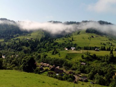 Uçan beyaz bulutlar ve küçük köy dağlarda. Doğal havadan görünümü