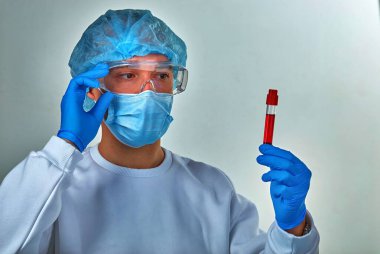 Maskeli doktor Coronavirus COVID19, HIV, ebola veya diğer tehlikeli enfeksiyonlar için kan test tüpüne bakıyor. Tıbbi geçmiş, enstrümanlar, şablon, duvar kağıdı. Coronavirus hastalığı konsepti