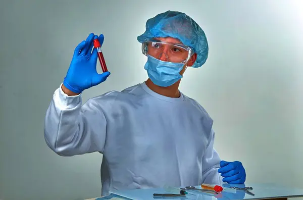 Doctor in mask performing blood test for coronavirus COVID19, HIV, ebola or other dangerous infection. Medical background, instruments, syringe, template, wallpaper. Coronavirus disease concept
