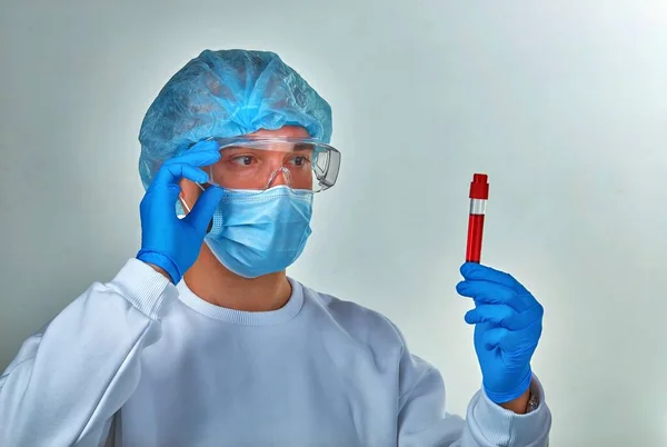 Doctor in mask looking at the blood test tube for coronavirus COVID19, HIV, ebola or other dangerous infection. Medical background, instruments, template, wallpaper. Coronavirus disease concept