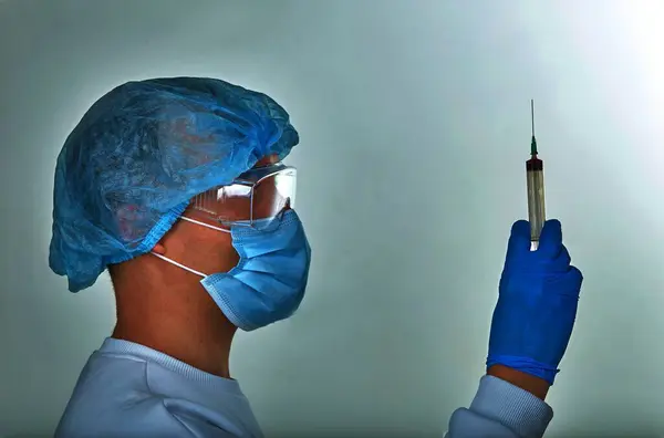 Doctor in mask performing blood test for coronavirus COVID19, HIV, ebola or other dangerous infection. Medical background, instruments, syringe, template, wallpaper. Coronavirus disease concept