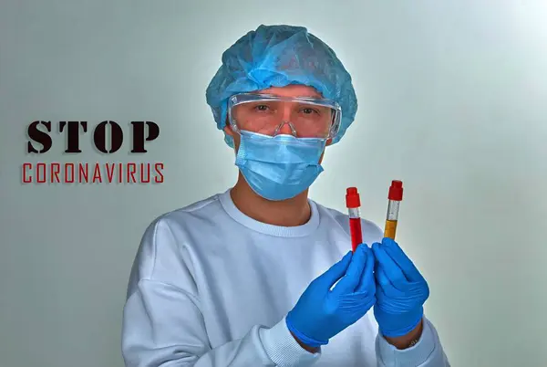 Doctor in mask looking at the blood test tube for coronavirus COVID19, HIV, ebola or other dangerous infection. Medical background, instruments, template, wallpaper. Coronavirus disease concept