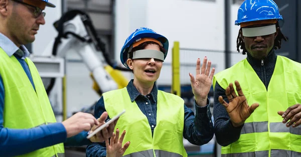 Team of engineers having simulation experience with futuristic virtual reality glasses inside robotic factory - Tech industry and metaverse concept