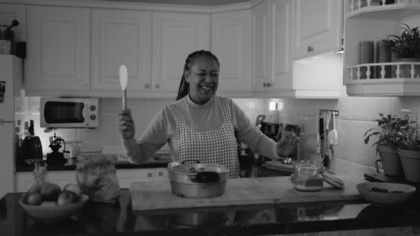キッチンで自家製デザートを準備しながら楽しいダンスをしている幸せなシニアアフリカの女性 黒と白の編集 — ストック動画