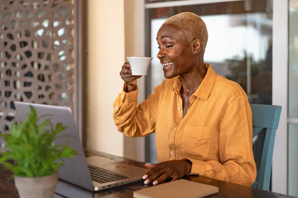 Happy African woman drinking a coffee while working with laptop at the cafe shop