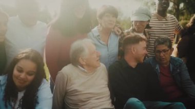 Mutlu çoklu nesiller halk parkında çimenlerde otururken eğleniyor.