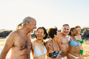 Mutlu çok ırklı kıdemli arkadaşlar yaz tatillerinde sahilde eğleniyorlar - çeşitli yaşlı insanlar tatilden zevk alıyorlar