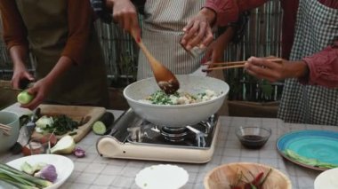 Güneydoğu Asyalı anne ve kızları ev verandasında Tayland yemeği tarifi hazırlarken eğleniyorlar.
