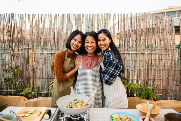 ハッピー東南アジアの家族は ハウスパティオで一緒にタイ料理レシピを準備しながら カメラの前に笑顔を持っています ストック写真