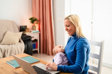 Mutlu anne küçük bebeği uyurken dizüstü bilgisayar kullanıyor.