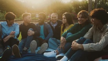 Halka açık bir parkta çimlerde oturarak eğlenen mutlu çoklu nesil insanları - çeşitlilik ve arkadaşlık kavramı