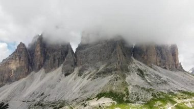 İkonik Tre Cime di Lavaredo tepeleri yeşil bir çayırda yükseliyor. Zirvelerin etrafında dönen beyaz bulutlar, Dolomitler, İtalya