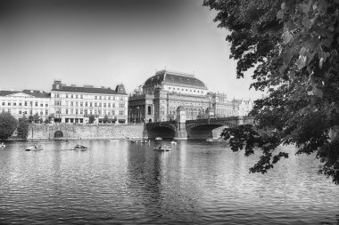 Prag 'daki Vltava nehrinin kıyısında oturan Ulusal Tiyatro, güneşli bir günde kürek çeken turistlerle birlikte.